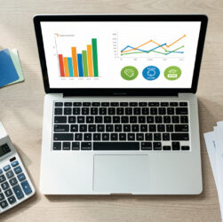 Espace de travail analytique montrant un ordinateur avec des graphiques abstraits, une calculatrice et des documents de budget pour évaluer la rentabilité de campagnes marketing.